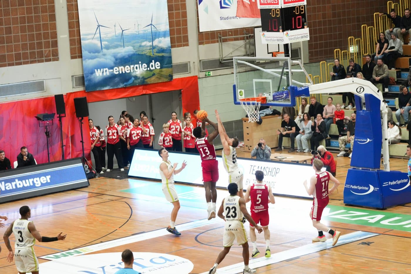 Spielszene der Paderborn Baskets unter dem Korb, im Hintergrund Fans auf der Tribüne
